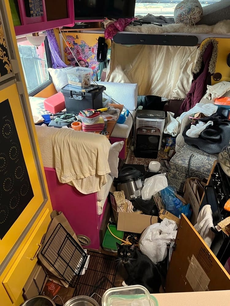 Photo shows the interior of an RV with piles of clothes, dishes, boxes, tools, and various containers and knick-knacks 